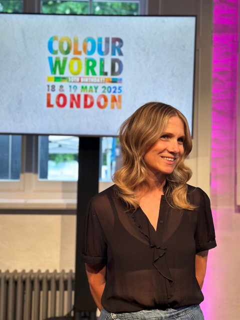 Woman: Vicki Borley, co-md at OCCS, standing in front of a screen displaying 'Colour World' event details in London.